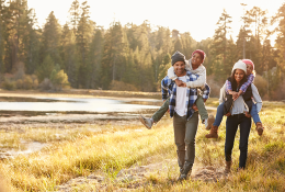 Parents Giving Children Piggyback Ride On Walk By Lake