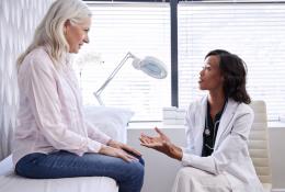 Mature Woman In Consultation With Female Doctor Sitting On Examination Couch