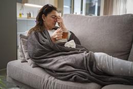 Sick woman sitting on couch with tea in her hand