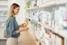 A woman peruses the shelf at a pharmacy, reading the label