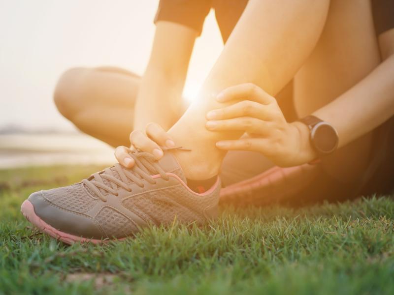 A person wearing running shoes sitting on grass bracing their ankle
