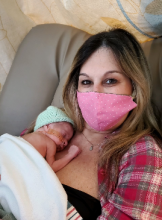 new mom with a pink medical mask holding newborn