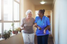 Senior woman who is very happy being helped down a sunny hallway with a smiling nurse