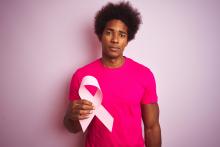 Male in a pink shirt holding a pink ribbon on a pink background