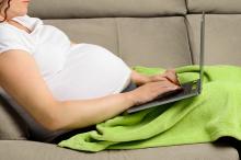 young pregnant woman using a digital laptop while relaxing on the sofa at home