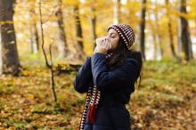 woman sneezing surrounded by fall foliage