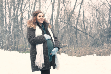 Beautiful Hispanic prenant woman with long curly red auburn hair wearing a green sweater, coat, scard and fingerless gloves standing in snow in a forest in late Autumn, Minnesota