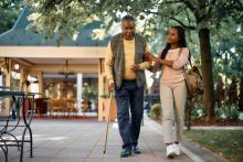 african american man walking with a cane and the assistance of a young woman
