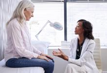 Mature Woman In Consultation With Female Doctor Sitting On Examination Couch