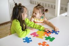 Funny girls collect puzzles together at the table in the children's room