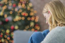 Woman sitting with head down in front of Christmas tree.