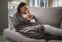 Sick woman sitting on couch with tea in her hand