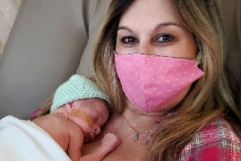 new mom with a pink medical mask holding newborn