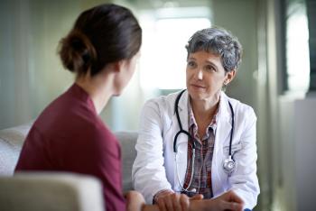 Older female doctor sitting and talking with younger female patient