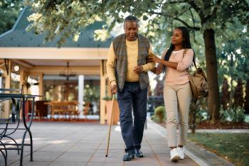 african american man walking with a cane and the assistance of a young woman