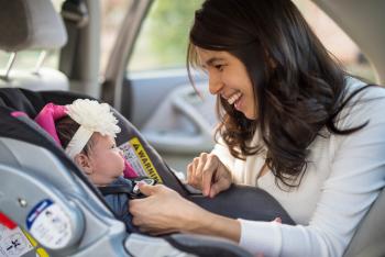 mother placing baby safely in car seat