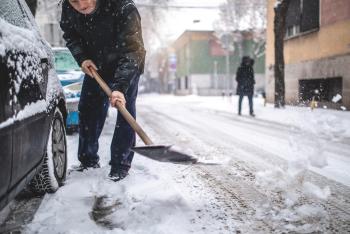 Man shoveling snow in street around cars.