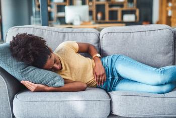 Woman laying on couch exhibiting stomach discomfort.