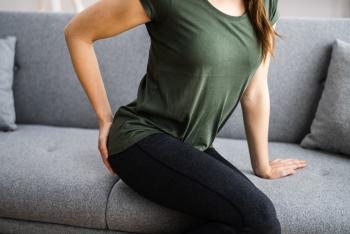 Woman sitting on couch while holding her lower back